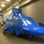 helicopter without rotors encased in blue aircraft shrink wrap ready for shipping