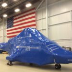 helicopter without rotors encased in blue aircraft shrink wrap ready for shipping