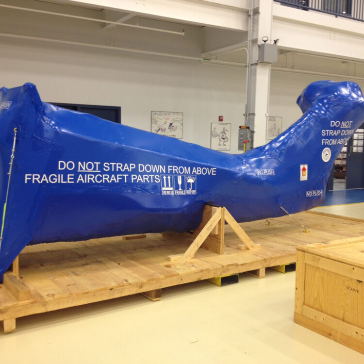 helicopter tail encased in blue aircraft shrink wrap secured to a wooden base